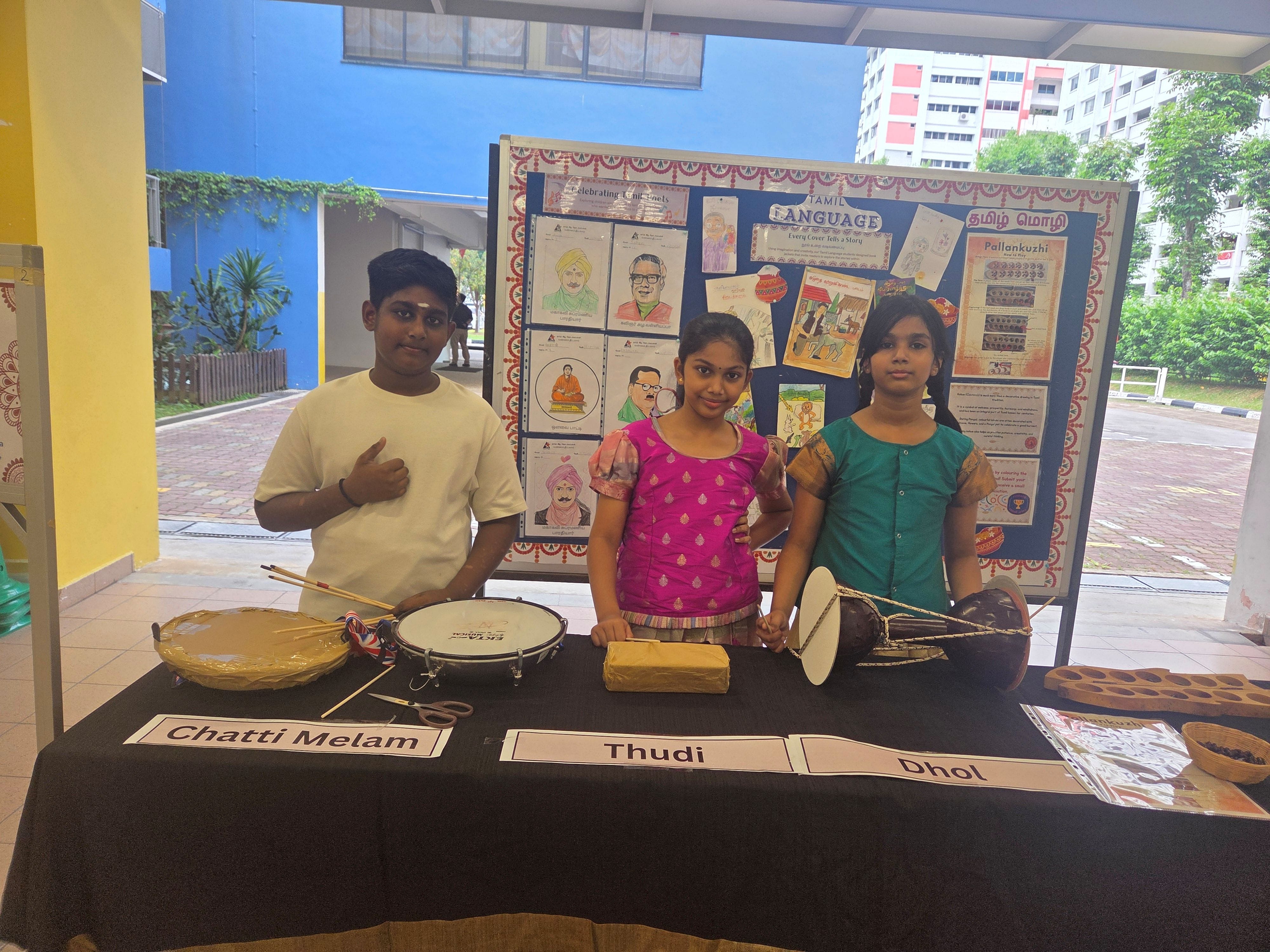 Three students sharing about the Indian musical instruments at a booth activity during mother tongue fortnightt week